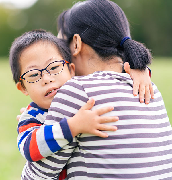 A portrait of a happy mother while she is hugging her small son with Down syndrome.